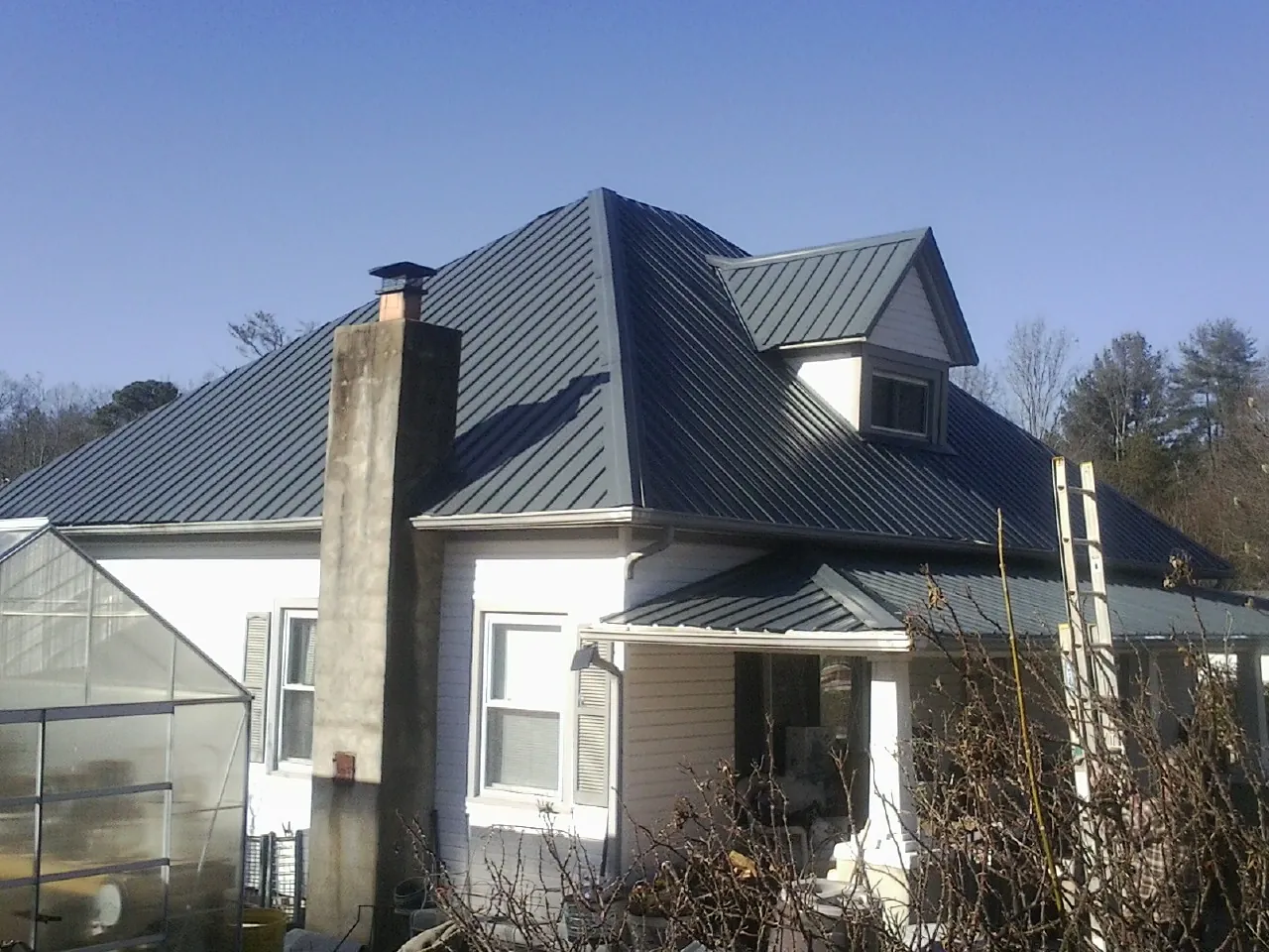 Dark blue standing seam metal roof on a white farmhouse with dormer — Slate & Tile Roof Repair by Roofing Brothers in Ellenton